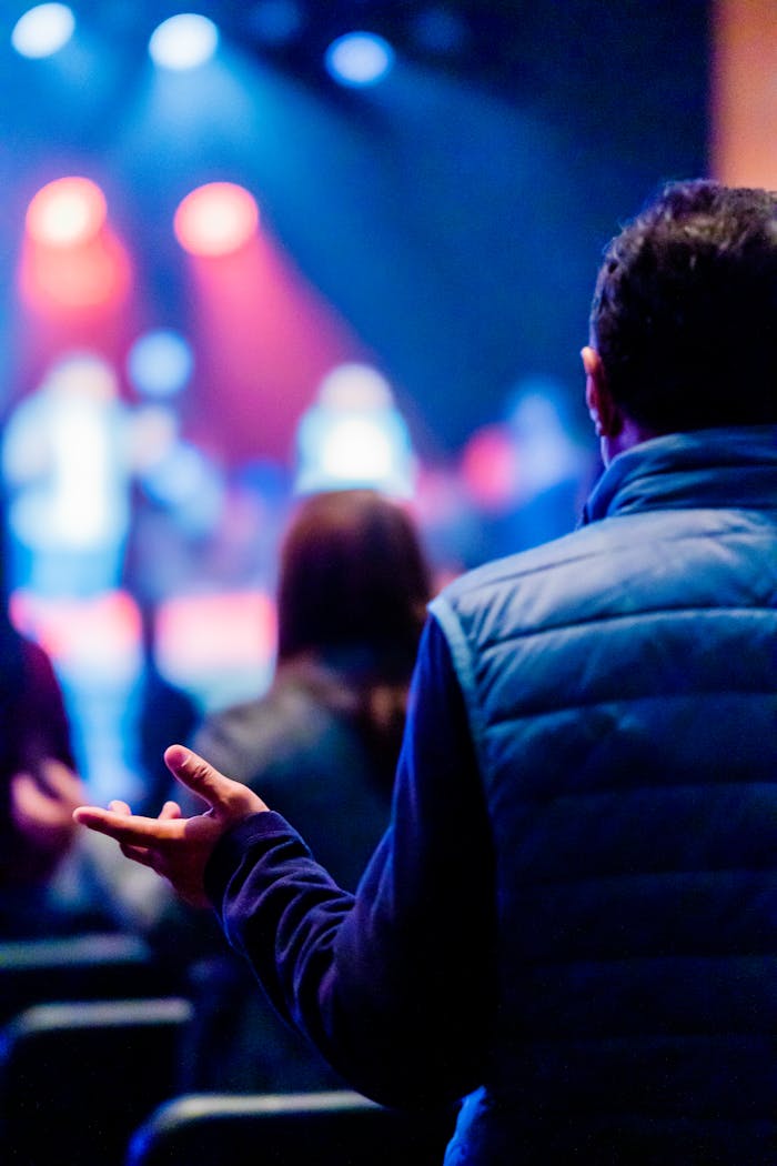 Audience at a worship concert, man praying, with vibrant stage lights.